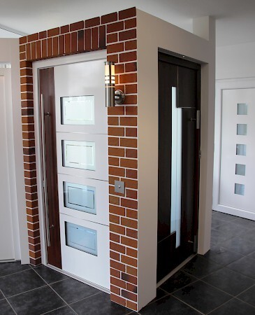 Moderne Haustür mit Glasfenstern und Klinkerrahmen in einem hellen Flur auf Fliesenboden.